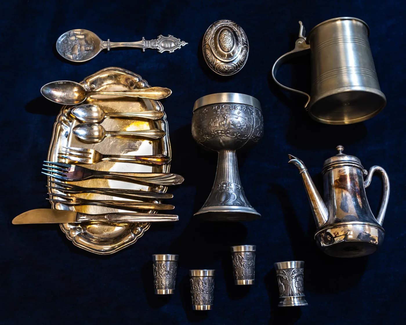 Silberbesteck, Pokal, Becher und Kanne auf dunklem Samt – Aufnahme von Juwelier Plottka